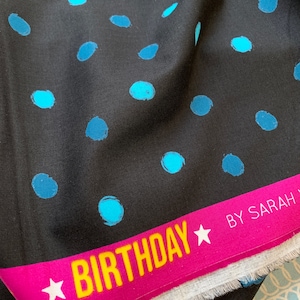 Könnte beinhalten: Schwarzer Stoff mit blauen Tupfen. Ein pinkfarbenes Band mit dem Wort "BIRTHDAY" in Gelb und weißen Sternen ist sichtbar. Geeignet für Näh- oder Bastelprojekte.