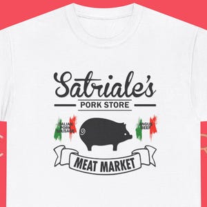 Könnte beinhalten: Weißes T-Shirt mit dem Text "Sabriale's Pork Store" über einer Schweinegrafik und den Worten "Meat Market". Das Design enthält italienische Flaggenakzente. Ein lässiges T-Shirt für Fleischliebhaber.