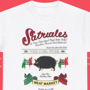 Könnte beinhalten: Weißes T-Shirt mit dem Text "Satriales" in einer stilisierten Schriftart, zusammen mit Grafiken eines Schweins und Details eines Fleischmarktes. Das Design enthält rote, grüne und weiße Akzente, die ein italienisches Thema andeuten.