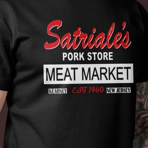Könnte beinhalten: Schwarzes T-Shirt mit einem weißen Aufdruck, der "Satriale's Pork Store Meat Market Kearny Est 1960 New Jersey" lautet.