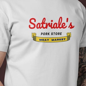 Könnte beinhalten: Weißes T-Shirt mit einem roten und gelben Logo, auf dem "Satriale's Pork Store Meat Market" steht.