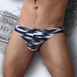 Pode incluir: Cueca de banho com padrão ikat em preto e branco. A cueca tem um corte baixo e acabamento branco. O fundo apresenta selos vintage e escrita manuscrita.