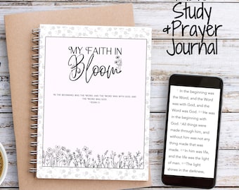 May include: A Bible Study and Prayer Journal with the title "My Faith in Bloom" is displayed on a wooden surface. The journal is open, revealing text and floral illustrations. A smartphone displays text, and a cup of coffee and glasses are also present.