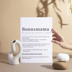Könnte beinhalten: Eine weiße Karte mit schwarzem Text, der das Wort "Bonusmama" als Nomen definiert, das eine Frau bezeichnet, die keine leibliche Mutter ist, aber ein Kind liebt und umsorgt, als wäre es ihr eigenes. Der Text enthält auch Synonyme für das Wort, wie "Herzensmama", "Lieblingsmensch" und "Familienheldin".