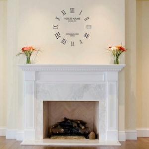 Może przedstawiać: Biały kominek z marmurową obudową i czarną naklejką zegara na ścianie nad nim. Naklejka zegara zawiera cyfry rzymskie i tekst "YOUR NAME CLOCK CO. ESTABLISHED 1998".