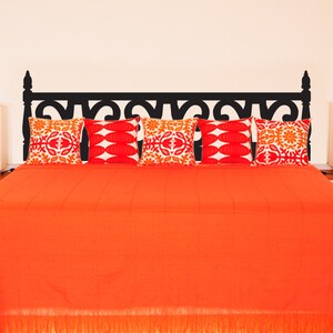 Puede incluir: Un adhesivo de cabecero negro con un dise&ntilde;o ornamentado, aplicado a una cama con un edred&oacute;n naranja y cinco almohadas de dise&ntilde;o. Las almohadas son blancas con dise&ntilde;os geom&eacute;tricos naranja y rojo.