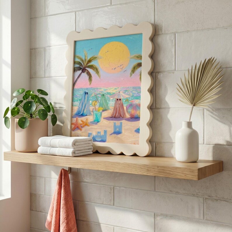 Tiny Ghosts Beach Day Wall Art displayed in a unique wavy cream frame on a wooden bathroom shelf next to a green plant and white towels. The playful pastel colors of the summer ghosts provide a cheerful contrast against the clean white tile wall in this bright maximalist interior. An ideal example of quirky bathroom art that transforms a functional space into a whimsical summer retreat... — bring warmth home.