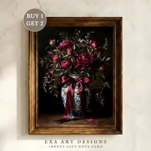 May include: A framed floral still life painting. The artwork features a vase filled with burgundy peonies and greenery, tied with a burgundy ribbon. The vase has a blue and white floral pattern. The frame is a warm, light brown color. The text "EXA ART DESIGNS + BONUS GIFT NOTE CARD" is at the bottom.