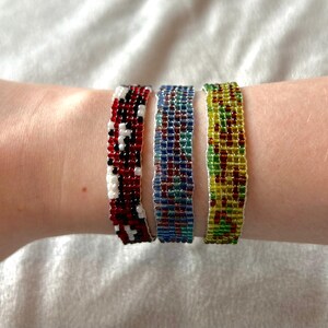 May include: Three beaded bracelets on a wrist. The bracelets are red and white, blue and green, and yellow and green.