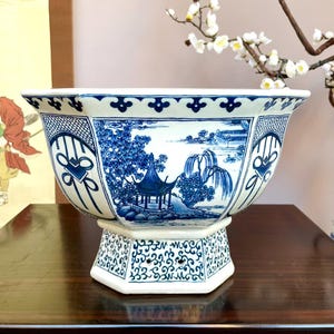 Könnte beinhalten: Großer, achteckiger Keramik-Blumentopf mit blau-weißem Landschaftsdesign. Der Topf zeigt eine detaillierte Szene einer Pagode, Bäume und Wasserfälle. Er steht auf einem passenden Sockel mit komplizierten Mustern.