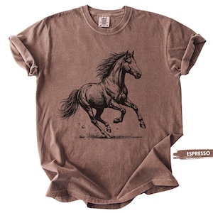 May include: Espresso-colored t-shirt featuring a detailed black illustration of a running horse. The horse is depicted with flowing mane and tail, kicking up dirt. The shirt has a classic crew neck and short sleeves.