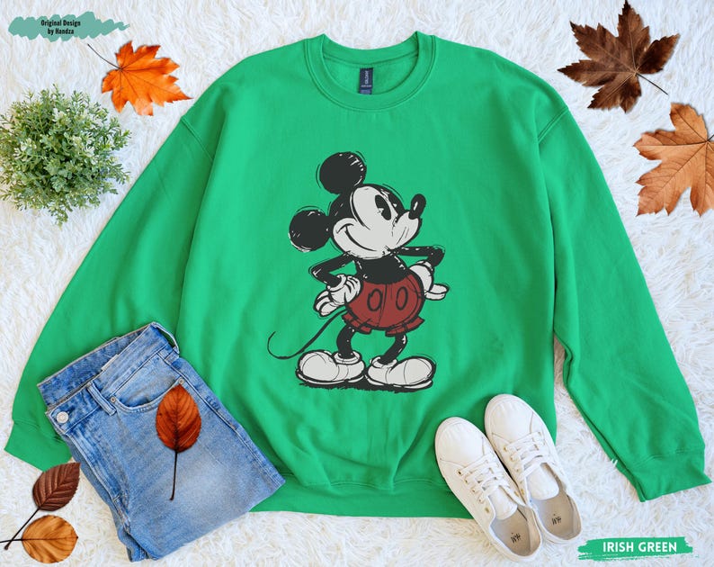 Puede incluir: Sudadera verde con un dise&ntilde;o de Mickey Mouse en negro, blanco y rojo. La sudadera se combina con vaqueros azules y zapatillas blancas. Las palabras "Irish Green" est&aacute;n impresas en la parte inferior derecha. El dise&ntilde;o es de estilo cl&aacute;sico de dibujos animados.
