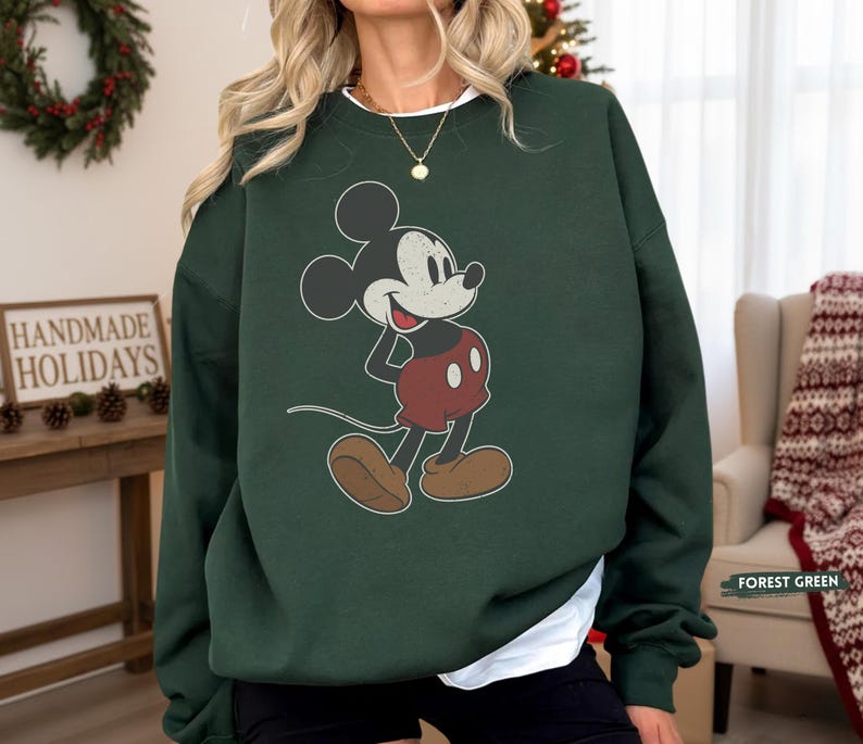 Puede incluir: Sudadera verde bosque con un dise&ntilde;o vintage de Mickey Mouse. El personaje de dibujos animados es de color negro, blanco, rojo y marr&oacute;n. La sudadera tiene cuello redondo y mangas largas. El texto "FOREST GREEN" es visible.