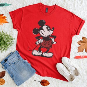 Puede incluir: Una camiseta roja con un dibujo de Mickey Mouse, combinada con vaqueros azules y zapatillas blancas. La palabra "RED" est&aacute; escrita en un rect&aacute;ngulo rojo. Ropa.