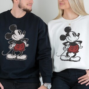 Puede incluir: Sudaderas azul marino y blancas con un gr&aacute;fico de Mickey Mouse desgastado. El personaje de dibujos animados est&aacute; representado en negro, rojo y blanco. Las sudaderas son de cuello redondo y manga larga.