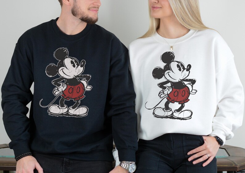 Puede incluir: Sudaderas azul marino y blancas con un gr&aacute;fico de Mickey Mouse desgastado. El personaje de dibujos animados est&aacute; representado en negro, rojo y blanco. Las sudaderas son de cuello redondo y manga larga.