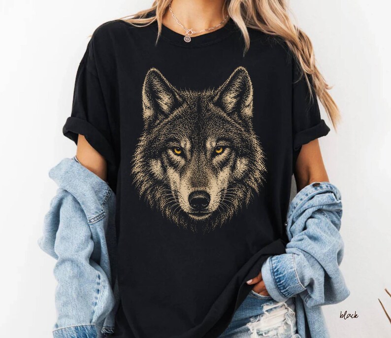 Puede incluir: Camiseta negra con una ilustraci&oacute;n detallada de la cara de un lobo. El lobo tiene ojos amarillos y un patr&oacute;n de pelaje detallado en tonos marrones y beige. La camiseta es de estilo cuello redondo cl&aacute;sico.