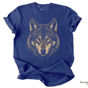 Puede incluir: Camiseta azul marino con una ilustraci&oacute;n detallada de la cara de un lobo. El pelaje del lobo est&aacute; representado en tonos marrones y beige, con ojos amarillos penetrantes. La camiseta es de material suave.