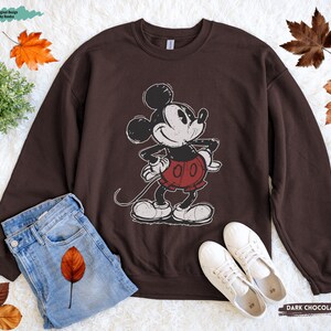 Puede incluir: Sudadera de color chocolate oscuro con un gr&aacute;fico desgastado de Mickey Mouse. El personaje de dibujos animados lleva su atuendo cl&aacute;sico, pantalones cortos rojos y guantes blancos. La sudadera se combina con vaqueros azules y zapatillas blancas.