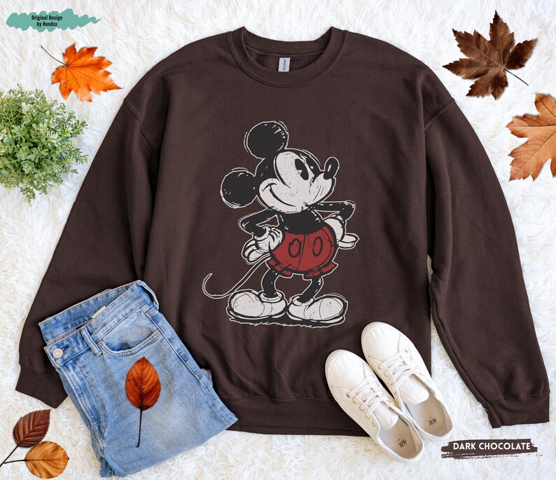 Puede incluir: Sudadera de color chocolate oscuro con un gr&aacute;fico desgastado de Mickey Mouse. El personaje de dibujos animados lleva su atuendo cl&aacute;sico, pantalones cortos rojos y guantes blancos. La sudadera se combina con vaqueros azules y zapatillas blancas.