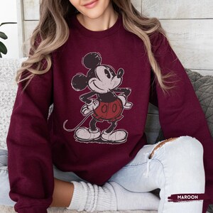 Puede incluir: Sudadera granate con un gr&aacute;fico desgastado de Mickey Mouse en negro, rojo y blanco. El personaje de dibujos animados est&aacute; de pie con las manos en las caderas. La palabra "MAROON" est&aacute; impresa en blanco en la parte inferior de la imagen.