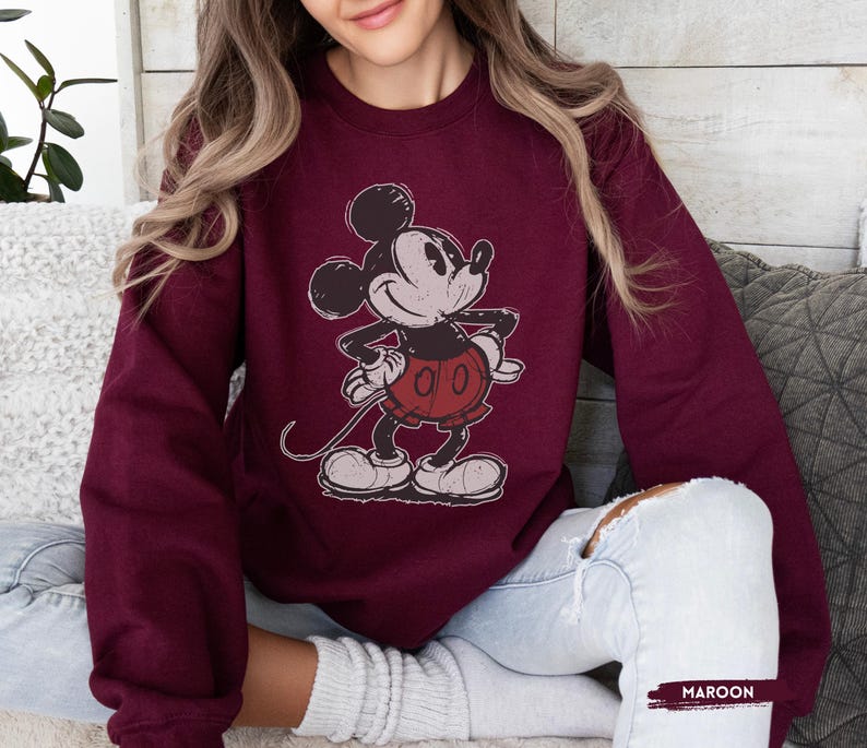 Puede incluir: Sudadera granate con un gr&aacute;fico desgastado de Mickey Mouse en negro, rojo y blanco. El personaje de dibujos animados est&aacute; de pie con las manos en las caderas. La palabra "MAROON" est&aacute; impresa en blanco en la parte inferior de la imagen.