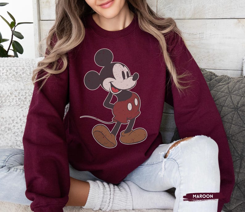 Puede incluir: Sudadera granate con un dise&ntilde;o de Mickey Mouse de estilo vintage. El personaje de dibujos animados se representa en su pose cl&aacute;sica, con pantalones cortos rojos y zapatos marrones. La palabra "MAROON" est&aacute; impresa en la esquina inferior derecha.