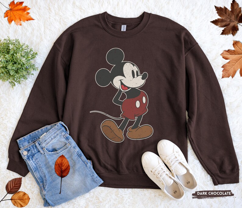 Puede incluir: Sudadera de color chocolate oscuro con un gr&aacute;fico de Mickey Mouse de estilo vintage. El personaje de dibujos animados est&aacute; representado en negro, rojo y marr&oacute;n. La sudadera se combina con vaqueros azules y zapatillas blancas, creando un look casual.