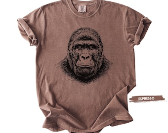 May include: Espresso-colored t-shirt featuring a detailed black illustration of a gorilla's face. The shirt has a crew neck and short sleeves with rolled cuffs. The fabric has a slightly faded appearance. The word "ESPRESSO" is printed on a brown rectangle.