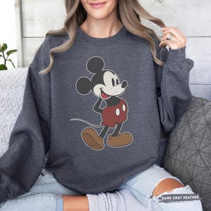 Puede incluir: Sudadera gris oscuro jaspeada con un dise&ntilde;o vintage de Mickey Mouse. El personaje de dibujos animados es de color negro, blanco y rojo, con zapatos marrones. La sudadera tiene mangas largas y el texto "DARK GRAY HEATHER" es visible.