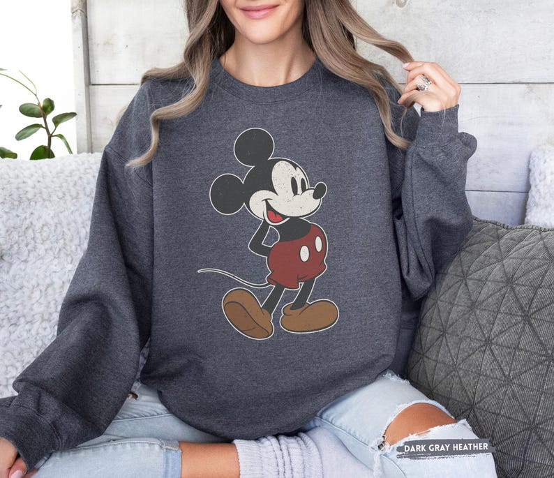 Puede incluir: Sudadera gris oscuro jaspeada con un dise&ntilde;o vintage de Mickey Mouse. El personaje de dibujos animados es de color negro, blanco y rojo, con zapatos marrones. La sudadera tiene mangas largas y el texto "DARK GRAY HEATHER" es visible.