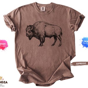 May include: Espresso-colored t-shirt featuring a detailed black illustration of a bison. The shirt has a classic crew neck and short sleeves. The image includes the text "UNIQUE Touch" and "FROM Designer".