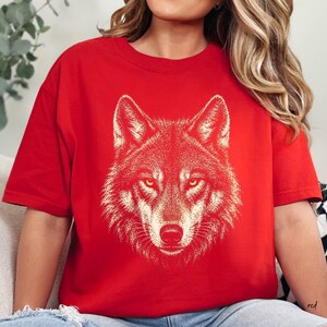 Puede incluir: Camiseta roja con una ilustraci&oacute;n detallada de la cabeza de un lobo. El pelaje del lobo se representa en un tono m&aacute;s claro, contrastando con el fondo rojo. El dise&ntilde;o est&aacute; centrado en la camiseta, mostrando la mirada intensa del animal.