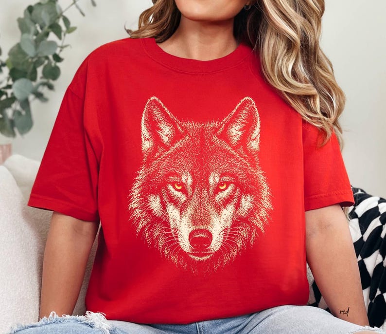 Puede incluir: Camiseta roja con una ilustraci&oacute;n detallada de la cabeza de un lobo. El pelaje del lobo se representa en un tono m&aacute;s claro, contrastando con el fondo rojo. El dise&ntilde;o est&aacute; centrado en la camiseta, mostrando la mirada intensa del animal.