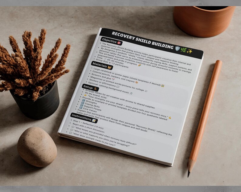 May include: A white document titled Recovery Shield Building with black text and emoji icons. The page outlines objectives, materials, setup, and instructions for an art-based activity. A wooden pencil lies beside the document on a flat surface.