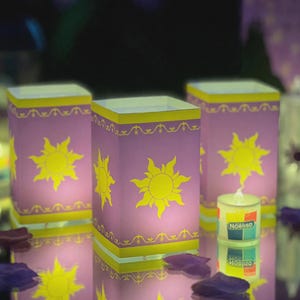 May include: Three square lanterns in light purple with yellow sun motifs and decorative borders. The text "not made of paper" is visible at the top. Each lantern features a bright yellow sun design on the front and sides, with yellow trim.