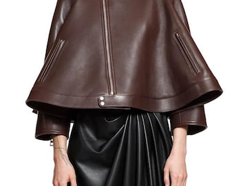 May include: A brown leather cape with a high collar and a silver zipper down the front. The cape has a layered design with a flared bottom and two zippered pockets. The garment is part of a fashion ensemble.
