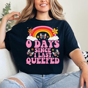 Puede incluir: Camiseta negra con un arcoíris, mariposas y el texto "0 Days Since I Last Queefed" en rosa.