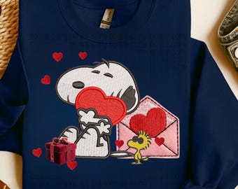 Könnte beinhalten: Marineblaues Sweatshirt mit gesticktem Snoopy, der ein rotes Herz hält. Ein rosa Umschlag mit einem Herz und Woodstock sind ebenfalls gestickt. Rote Herzen und eine Geschenkbox vervollständigen das Design.