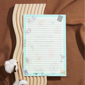 May include: A light blue notepad with lined pages and travel-themed illustrations. The notepad features the text "To travel is to take a journey to yourself". The notepad is decorated with stamps, a camera, and a compass.