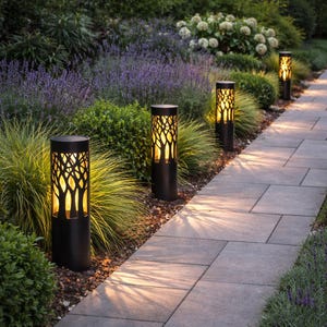 Puede incluir: Luces de camino exteriores cilíndricas negras con un diseño de ramas de árbol. Las luces están espaciadas uniformemente a lo largo de un camino de piedra, iluminando la vegetación circundante. Las luces miden aproximadamente 76 cm de alto.