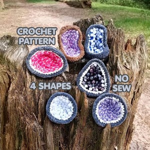 May include: Six crocheted geode-shaped items in various colors including pink, purple, blue, and white, with dark grey borders. Text on the image reads CROCHET PATTERN, 4 SHAPES, and NO SEW. The items are arranged on a textured, weathered tree stump.