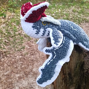 May include: A handmade crochet plush toy of a sea creature, primarily in shades of gray, white, and burgundy. The toy has a detailed design with white accents and yellow eyes. It is perched on a wooden surface, with a blurred natural background.