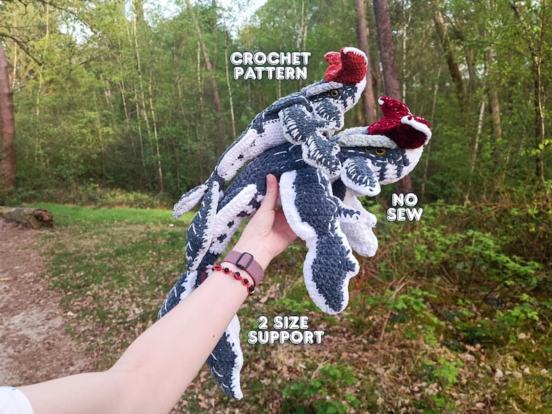 May include: Crocheted dinosaur toys in shades of gray and white, with red accents on their heads. The toys are held up in front of a blurred green background. Text on the image reads "CROCHET PATTERN", "NO SEW", and "2 SIZE SUPPORT".