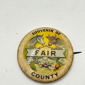 May include: Vintage souvenir pin from the County Fair. The round pin features a horse and a bull, with the word "FAIR" in a banner. The pin also has the words "SOUVENIR OF COUNTY" around the edge. The pin has a pin back.