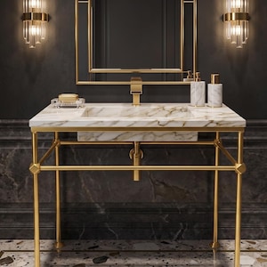 Puede incluir: Un lujoso mueble de baño con encimera de mármol y estructura metálica dorada. El mueble incluye un grifo dorado, un espejo a juego y lámparas decorativas. También se ven dispensadores de jabón y loción.