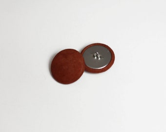 May include: Two brown suede buttons with a metal shank. The buttons are round and have a smooth surface.