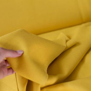 May include: A close-up of a bright yellow fabric being held by a hand. The fabric is soft and smooth, with a slight sheen.