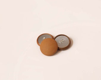 May include: Three round buttons with a light brown fabric cover and a silver metal back. The buttons have a wooden rim and are arranged on a white background. These buttons are suitable for sewing and craft projects.