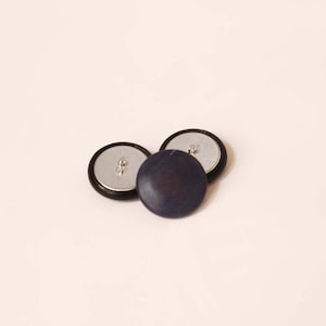 May include: Three round buttons, two are black with a silver center and one is a dark blue button.